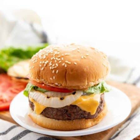 cheese stuffed burgers on a bun with onion, cheese, tomato, and lettuce on a white plate