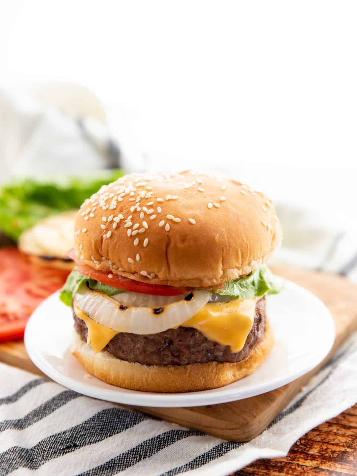 cheese stuffed burgers on a bun with onion, cheese, tomato, and lettuce on a white plate