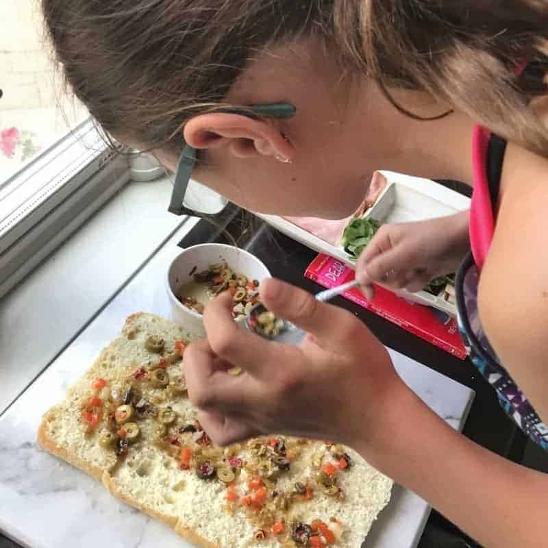  A small girl is spreading olive salad onto bread.