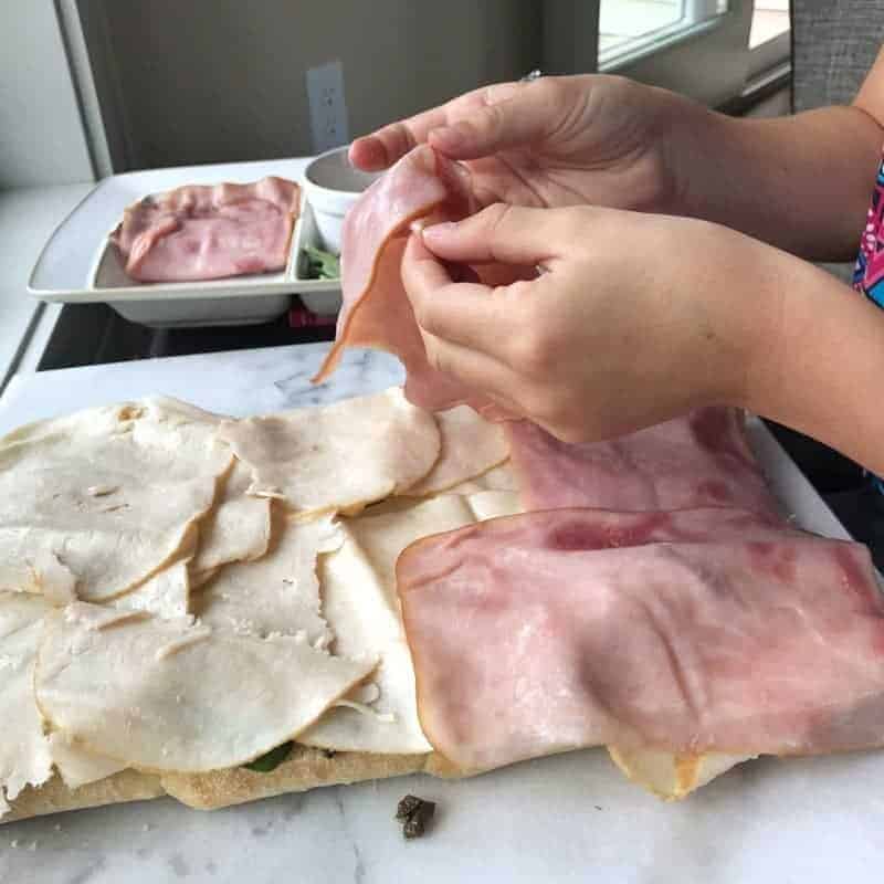 ham and turkey being placed onto a sandwich by a child.
