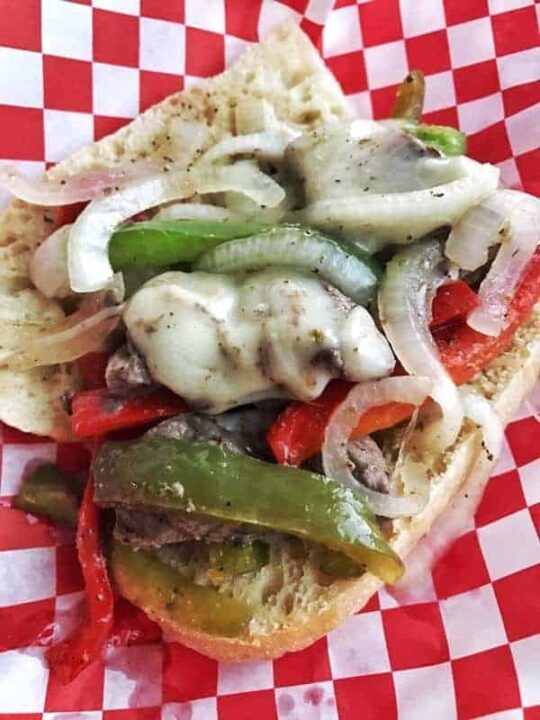 A Philly cheesesteak with lots of peppers on a bun. 