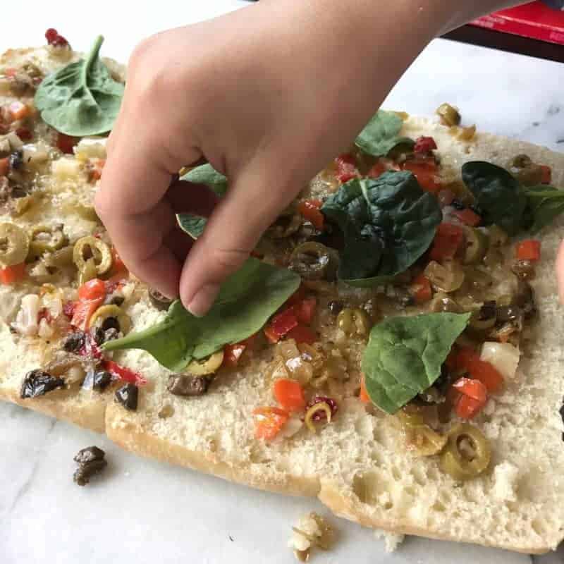 A Childs hand is placing spinach onto bread.