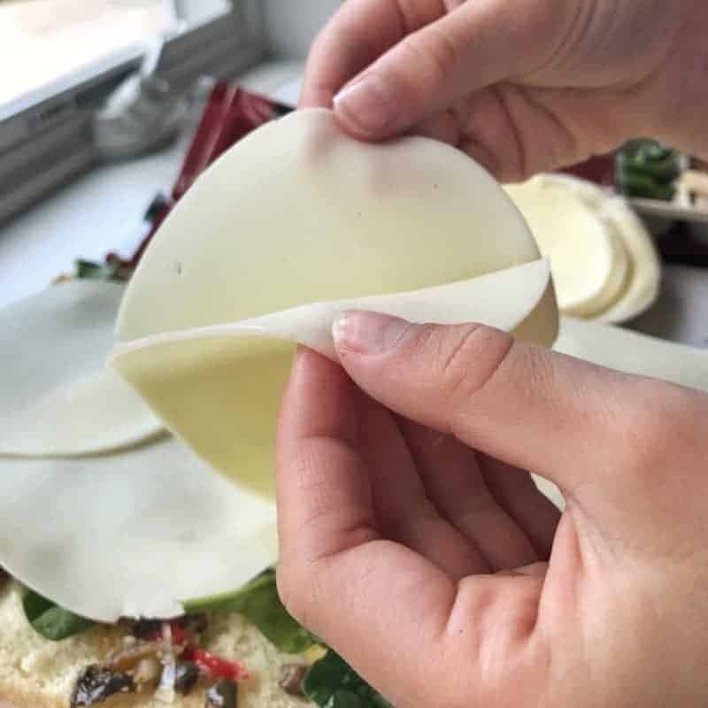 A childs hand is pulling two slices of provolone apart.