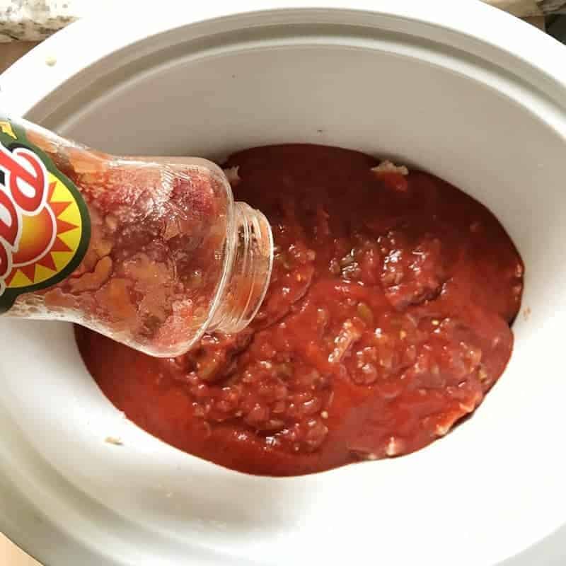 Homemade crock pot pasta being made in a white crock pot with salsa being added.