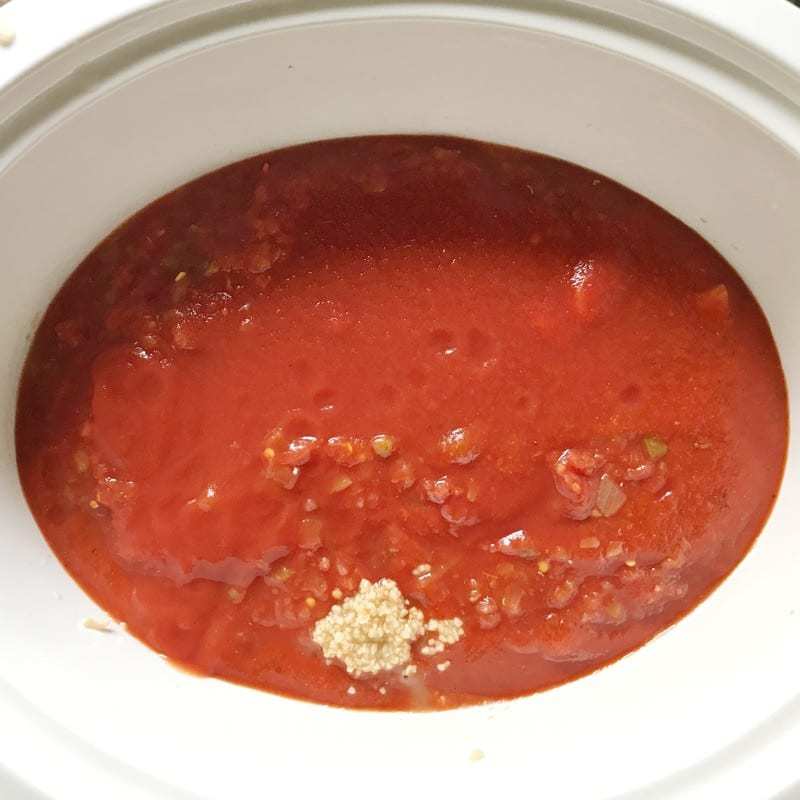 Crock pot spaghetti being made. Tomato products and garlic shown in a white crockpot.