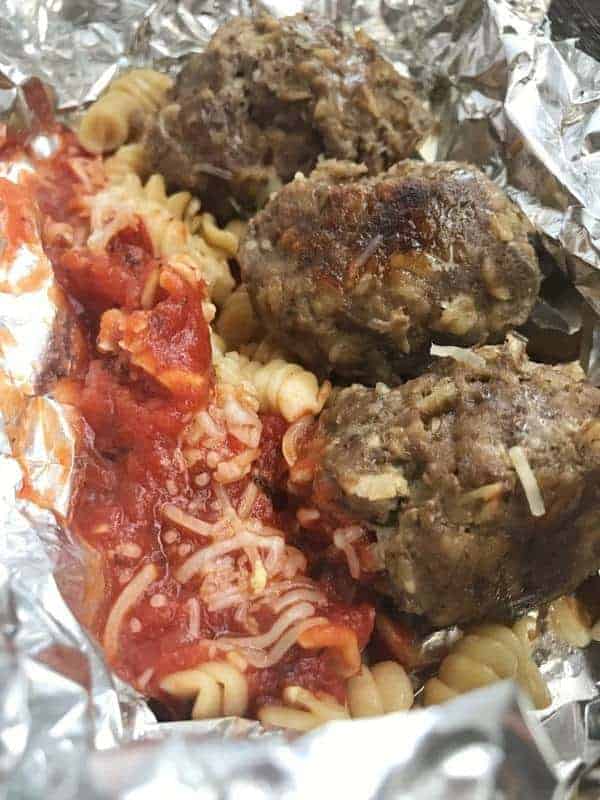 3 meatballs shown with pasta and sauce in a foil pack. 