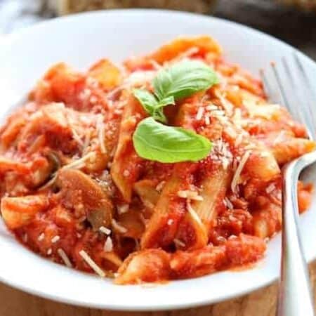 Chicken pasta with red sauce and mushrooms shown in a white bowl with fresh basil garnish and a fork.