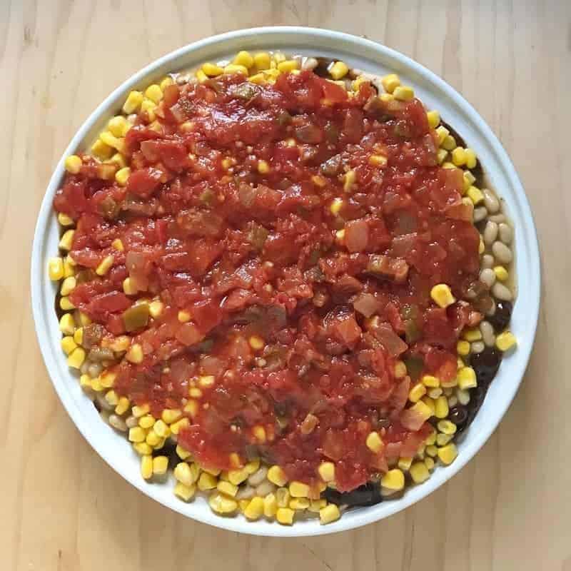 Seven layer bean dip showing the salsa layer in a white pie pan. 