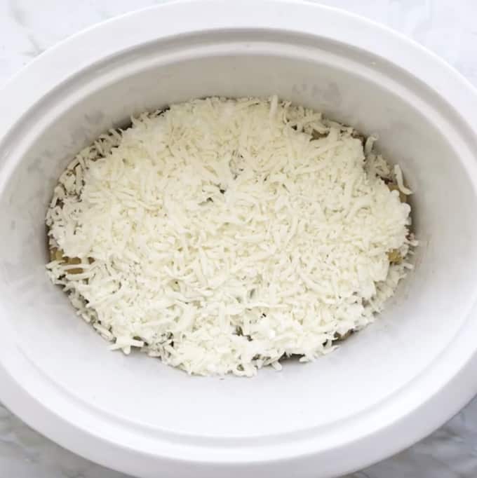Browned beef, noodles, cottage cheese and shredded mozzarella cheese added to the bottom of a white slow cooker.