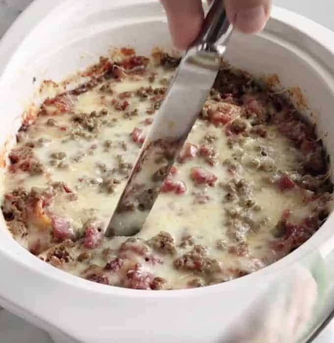 slow cooker lasagna is cooked and being sliced with a large knife.