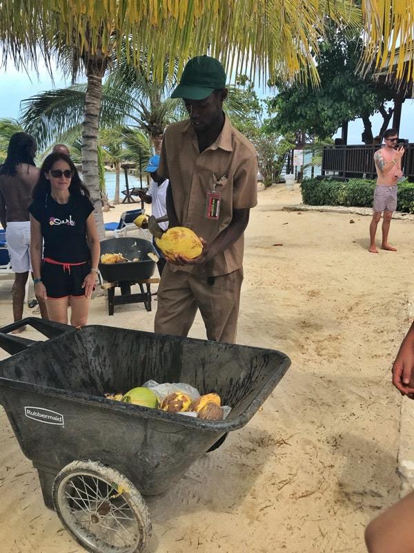 A man with a wheel barrow of coconuts slicing them open with a machete for guests.