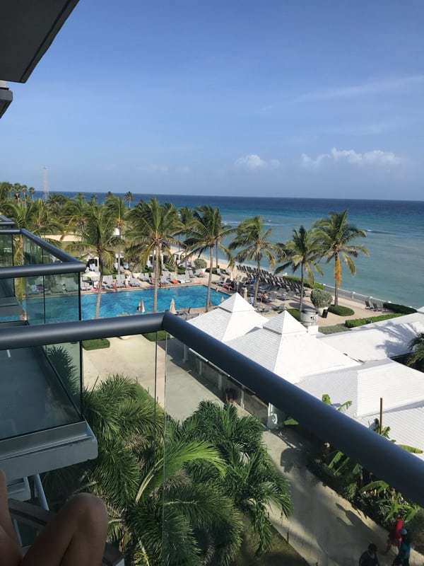 A view from the balcony at the Hilton Rose Hall over looking the Caribbean Sea, palm trees, and a pool.