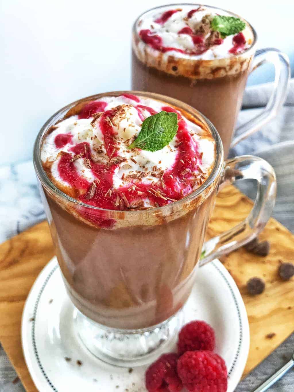 a clear mug of hot chocolate with raspberry drizzled on top