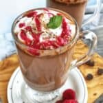 a clear mug of hot chocolate with raspberry drizzled on top