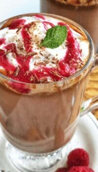 a clear mug of hot chocolate with raspberry drizzled on top