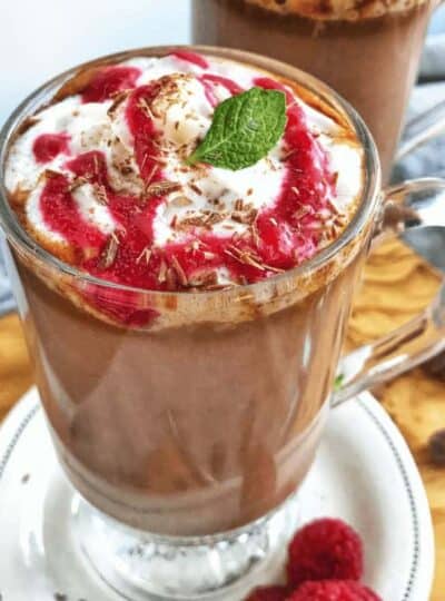 a clear mug of hot chocolate with raspberry drizzled on top