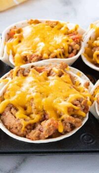 A 6 muffin tin with taco cups filed with meat and cheese after baking.