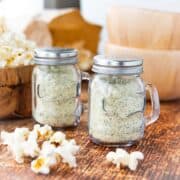 two glass salt shakers filled with ranch popcorn seasoning on a wooden surface.