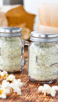 two glass salt shakers filled with ranch popcorn seasoning on a wooden surface.