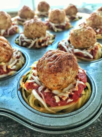 spaghetti and marinara sauce with meatballs in a 12 cup muffin tin.