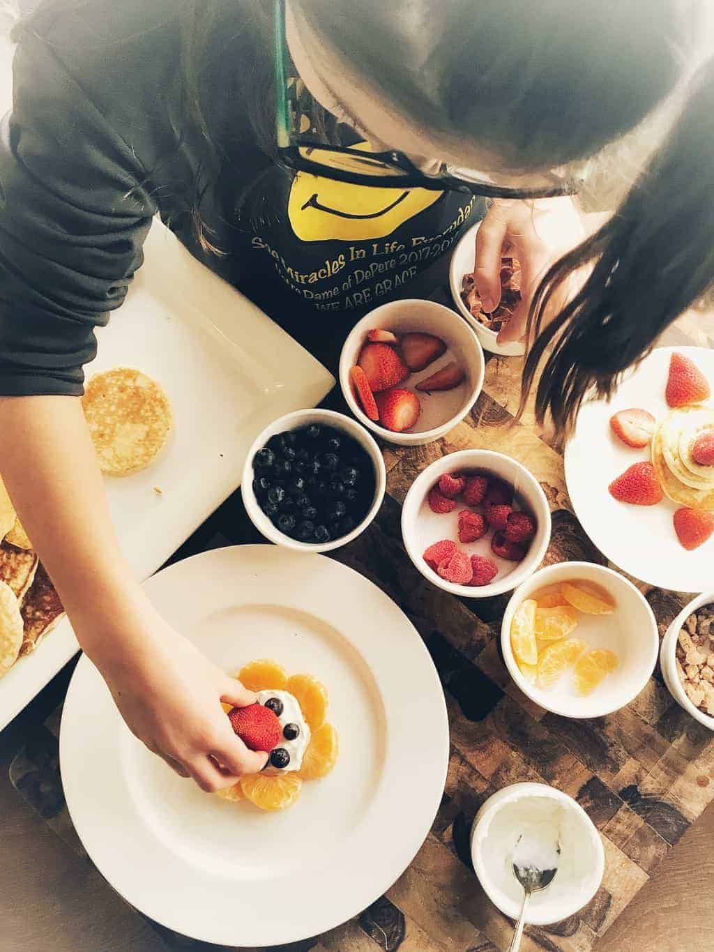 A girl decorating a Pancake with fruit