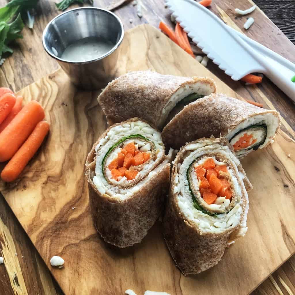 A turkey roll up is shown sliced on a wooded surface. Inside is turkey, spinach, and carrots.