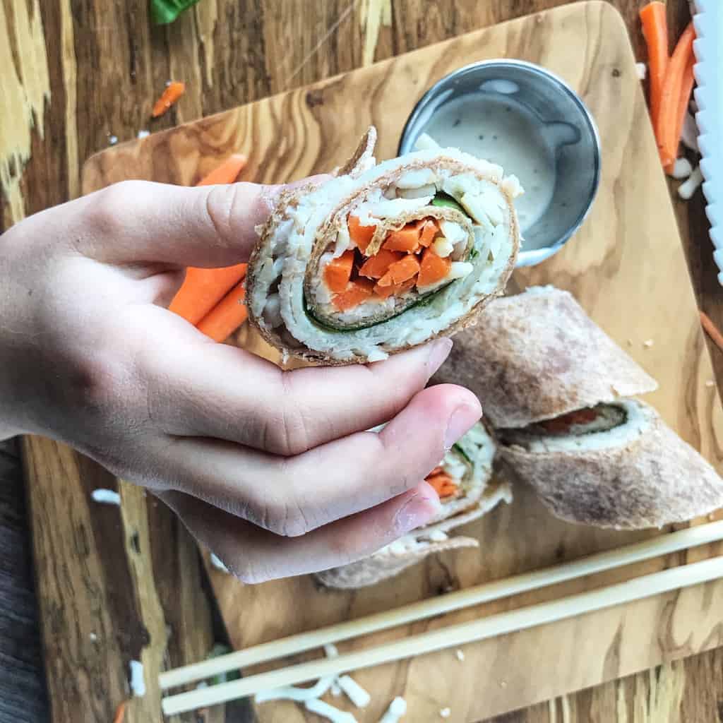 A Childs hand is holding a turkey roll up slice.
