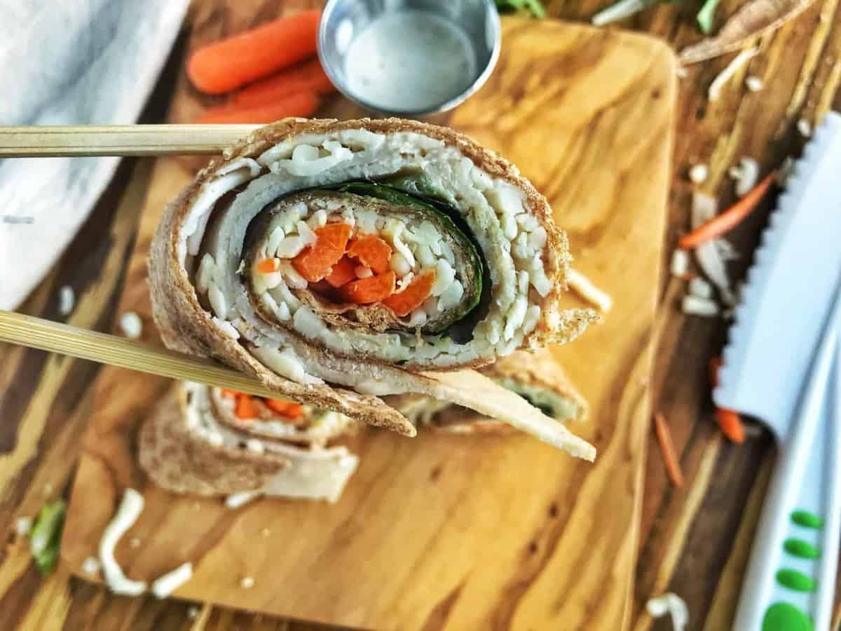 A slice of a turkey roll up is held with chopsticks. Inside is turkey, spinach, and carrots.