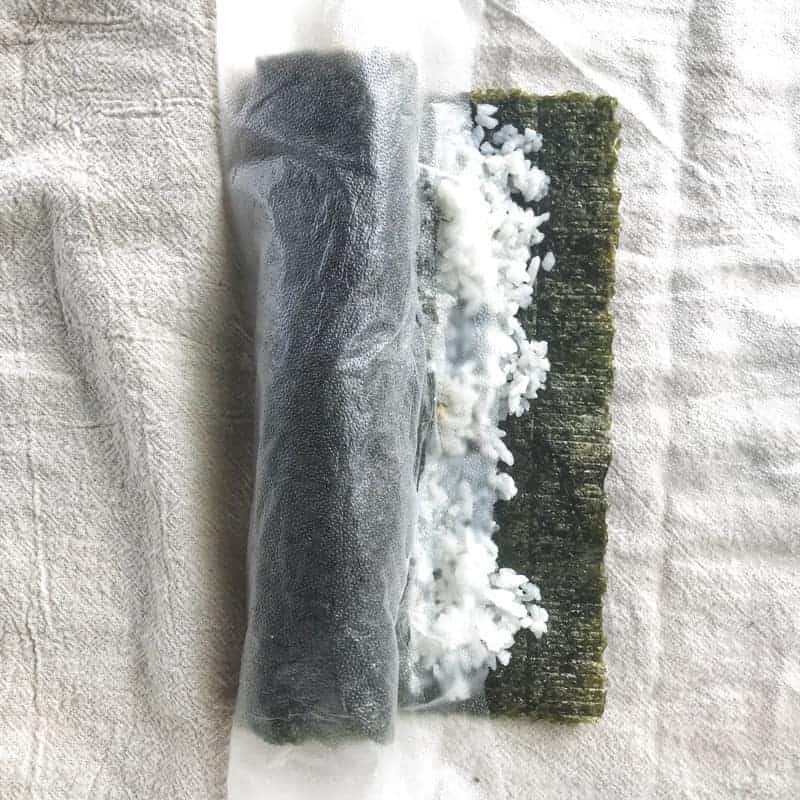 tuna sushi roll being rolled on a white surface.