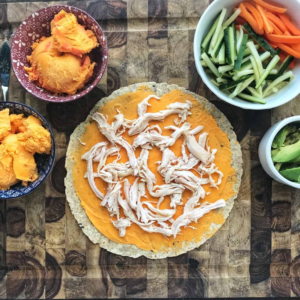 A flour tortilla is spread with cheese spread and topped with shredded chicken.