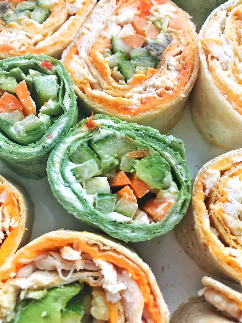 Pinwheels shown up close with cucumbers, avocado, cheese spread and carrots.