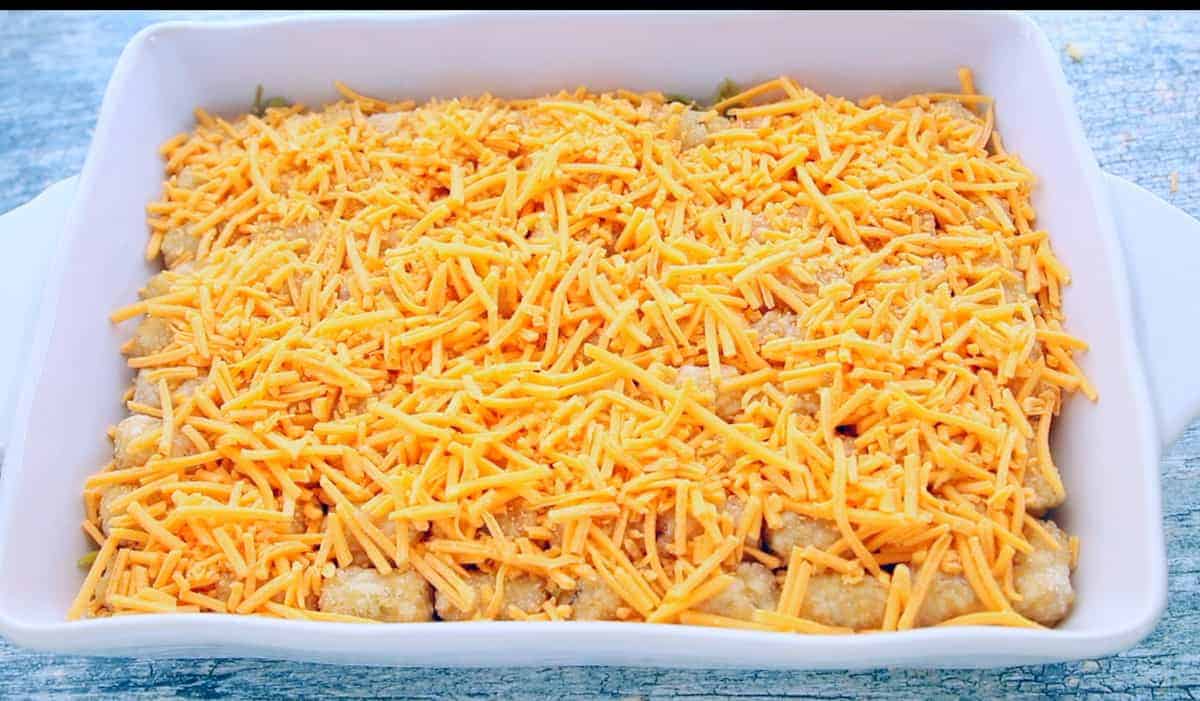 a baking dish is filled with the beef mixture topped with frozen tater tots topped with shredded cheese.