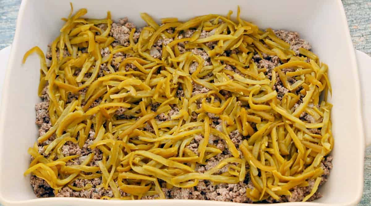 Tater Tot Casserole Recipe showing a baking dish filled with the beef mixture with a can of green beans over the top.