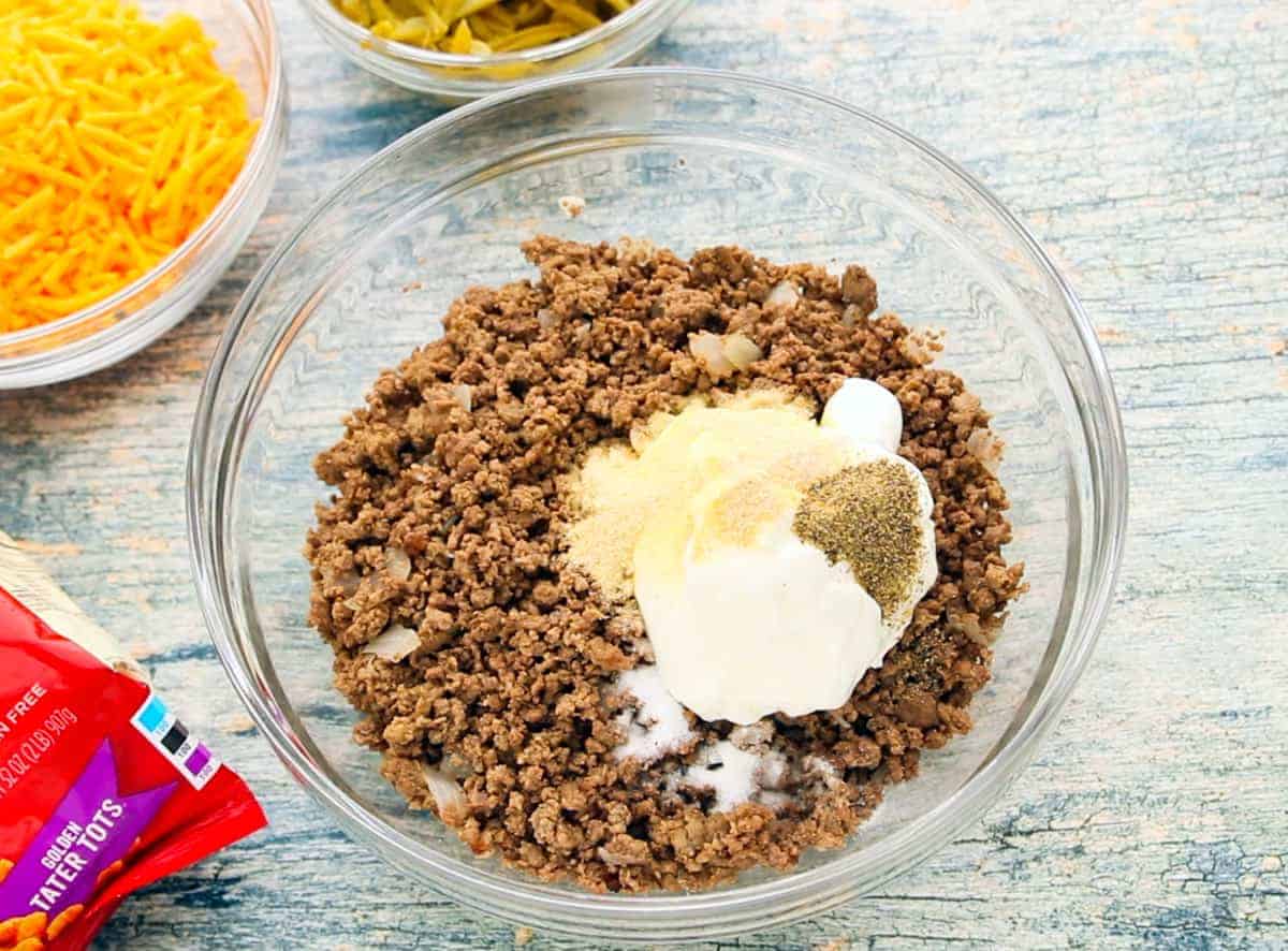 Tater Tot Casserole Recipe showing glass bowls filled with ingredients and a bag of frozen tater tots all on top of a wooden countertop.