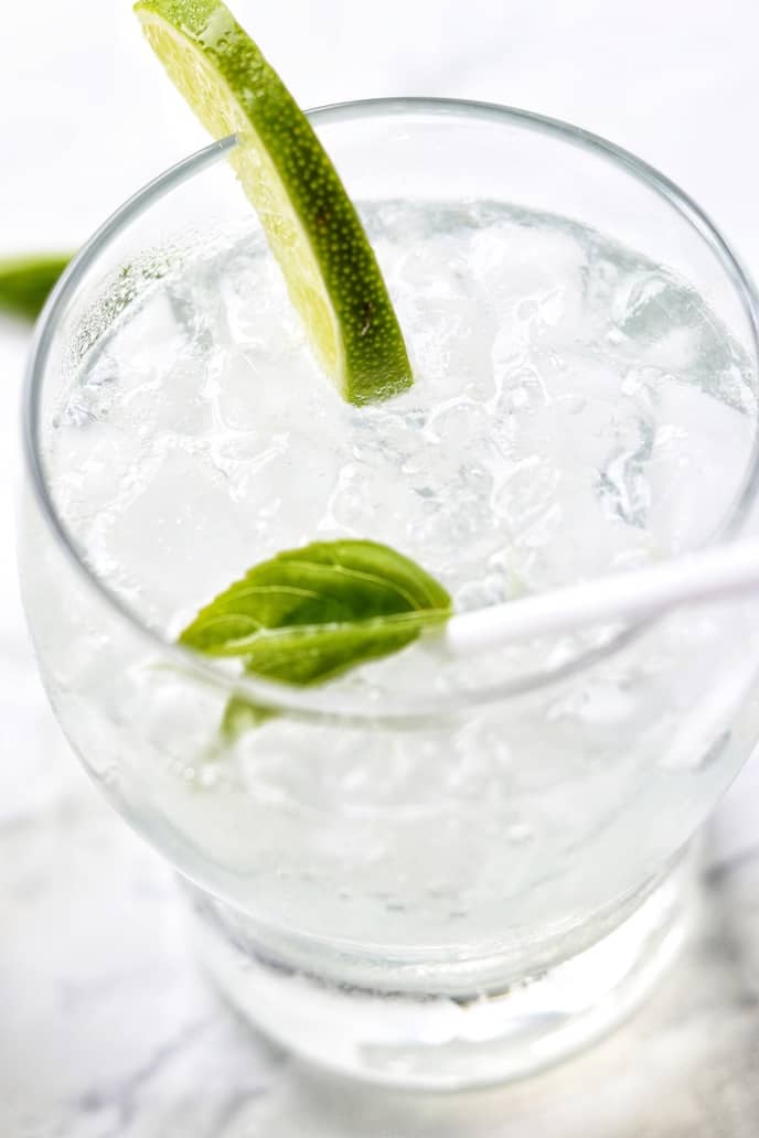 Close up of a homemade soda in a clear glass with lime and a straw.