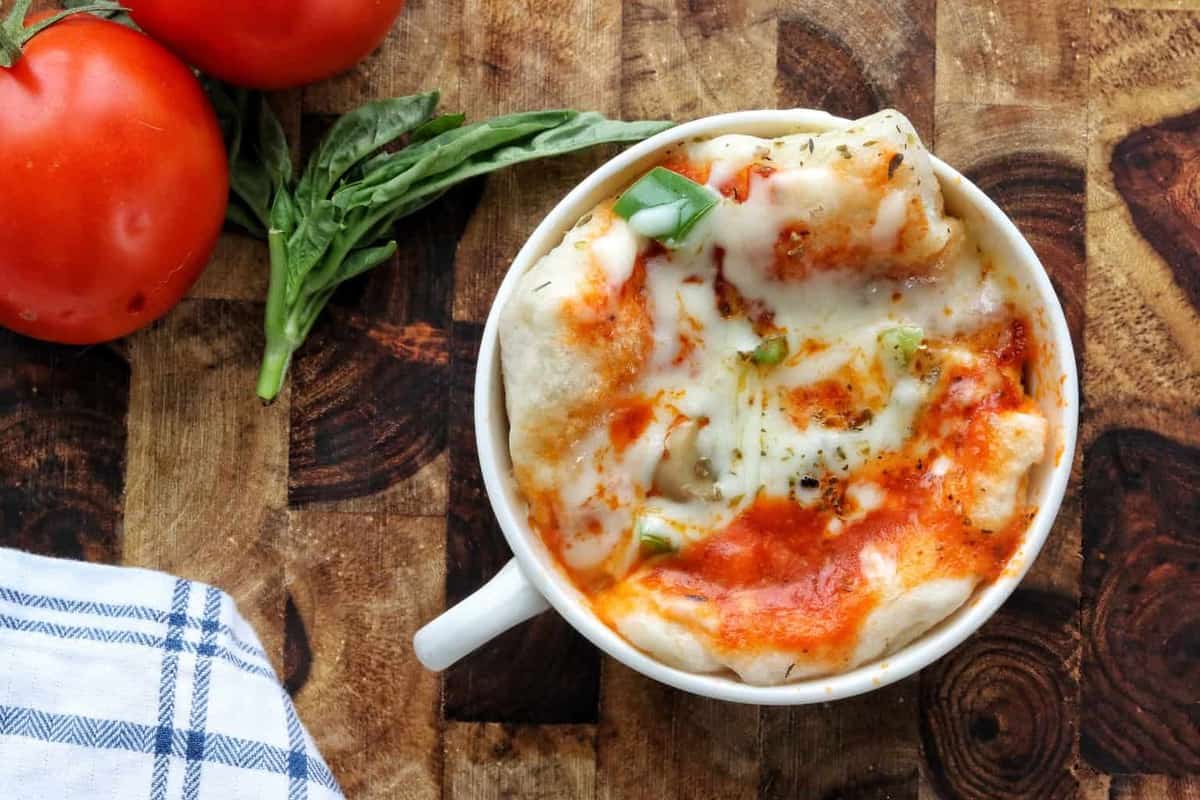 microwave pizza shown in a mug with melted cheese and peppers.