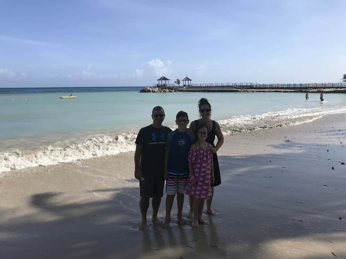 Picture of a family with a mom, dad, son, and daughter on the beach in front of the Caribbean ocean.