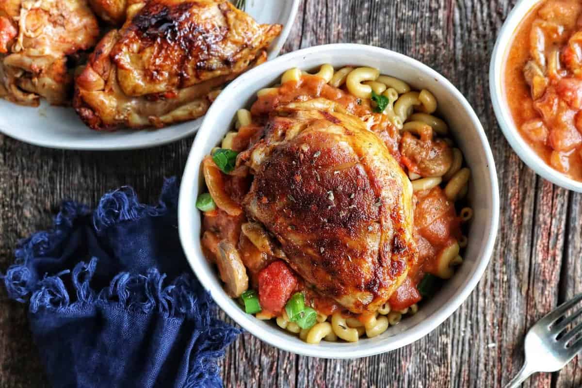 chicken cacciatore shown top down in a white bowl on top of elbow pasta.