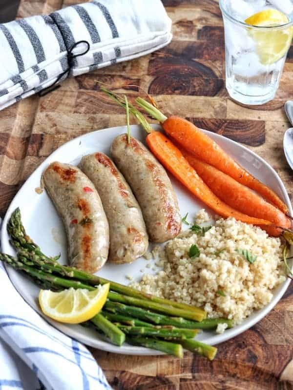 a white plate with chicken sausage, carrots, asparagus and rice.