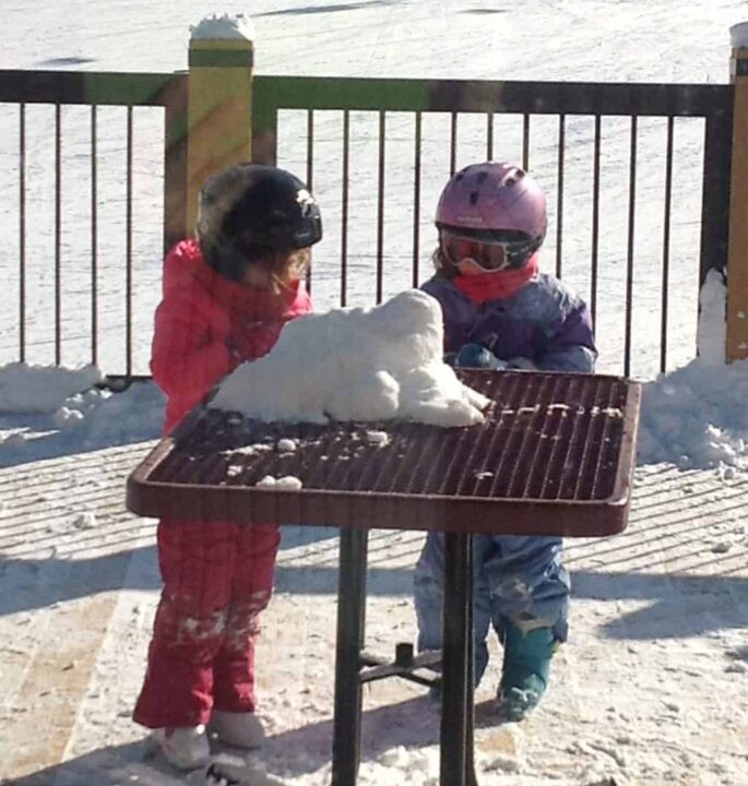 little girls in ski gear playing with snow