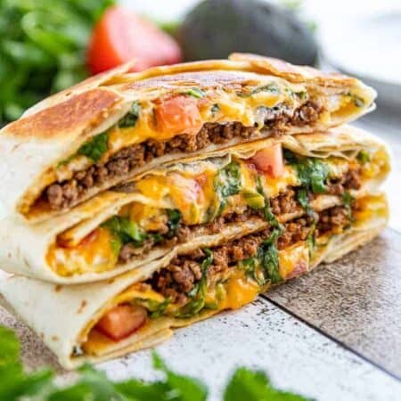 three stacked Crunchwrap supremes with beef and cheese oozing out.