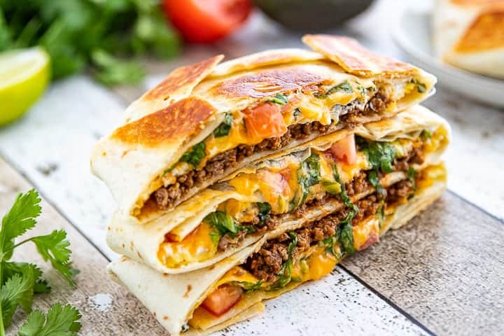 Crunchwrap Recipe shown cut in half with ground beef, tomatoes, lettuce and cheese showing stacked up three high.