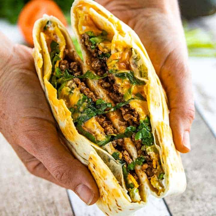 Crunchwrap supreme recipe shown cut in half with two hands folding it open where its sliced. 