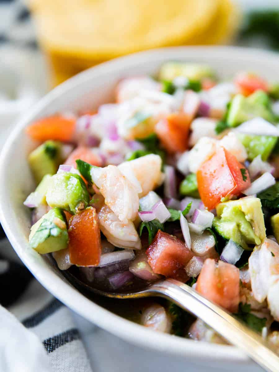 Diced shrimp, avocado, red onion, tomatoes and cilantro in a bowl with a spoon. 