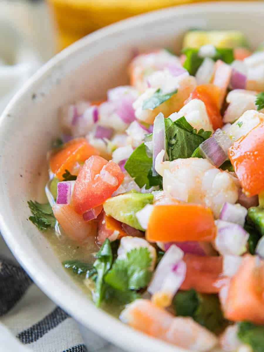 Shrimp Ceviche in a white bowl shown up close with sliced shrimp, avocado, fresh tomatoes, cilantro, and hot sauce.