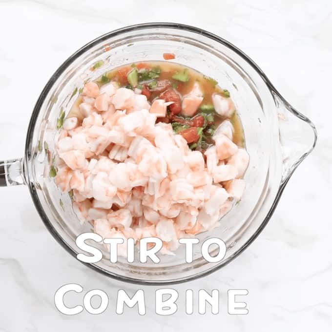 Chopped cooked shrimp is added to a clean mixing bowl with the vegetables from the ceviche recipe. The words Stir to Combine are on the bottom.