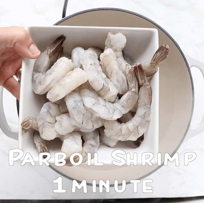 Raw shrimp getting ready to be parboiled in pot of boiling water in a large white pot.