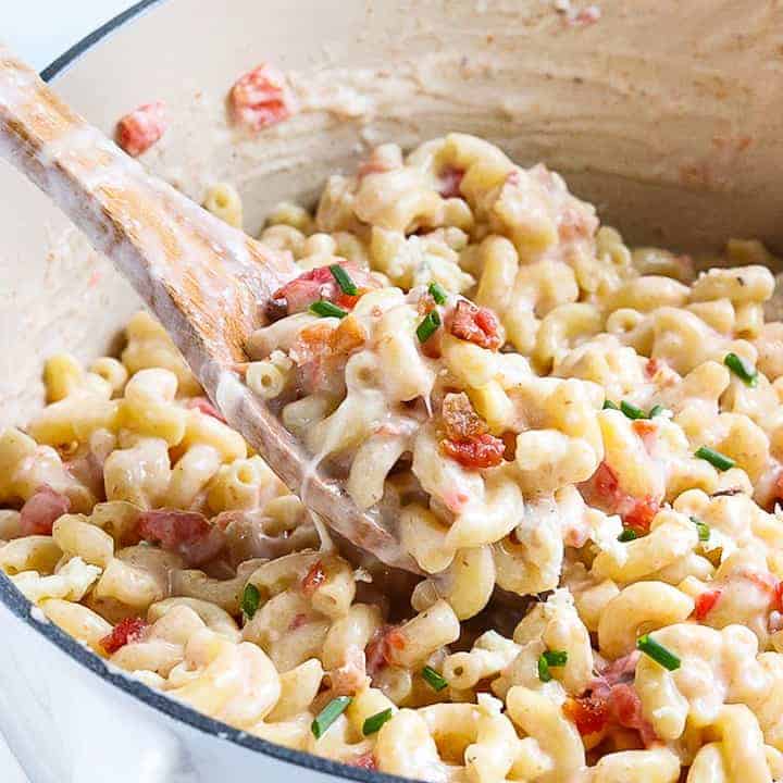 blue cheese mac and cheese with bacon shown in a white dutch oven with a wooden spoon showing the creamy pasta