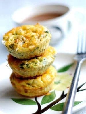 3 egg muffins stacked on top of each other on a white plate with a flower painted on it next to a fork and a cup of coffee blurred in the background.