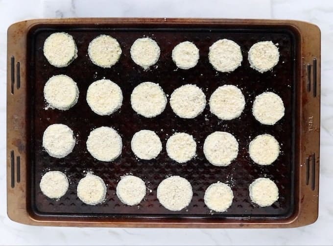 Coated zucchini rounds are shown on a baking tray ready to be cooked.
